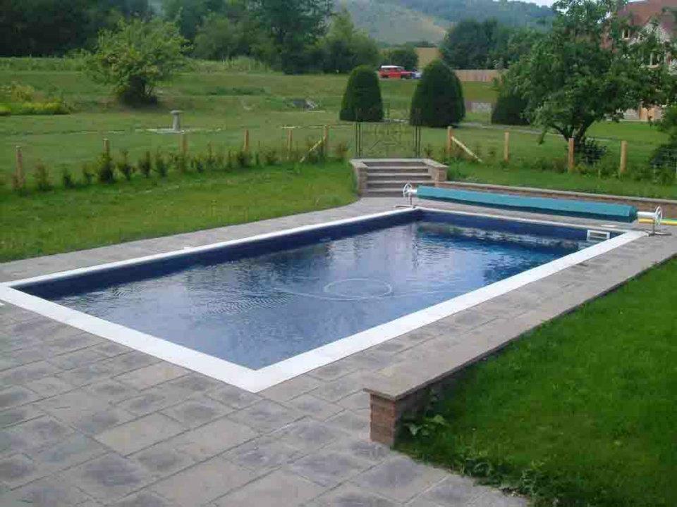 Rectangle outdoor swimming pool with pool cover. Surrounded by patio and grass