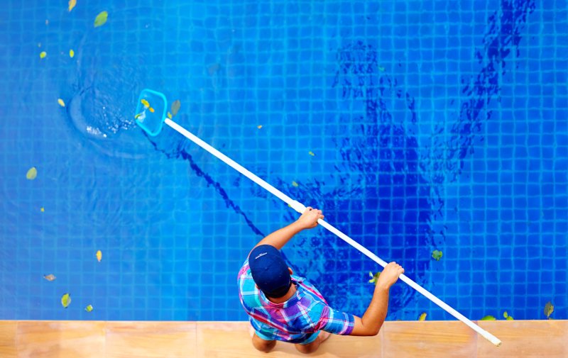 Pool & Spa Service Engineer cleaning a swimming pool with leaves in it