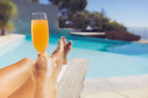 Person with orange drink in a flute glass next to a swimming pool