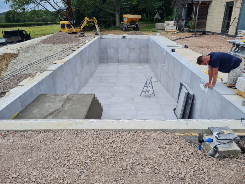 New swimming pool construction with men fitting tiles and diggers digging out surrounding area