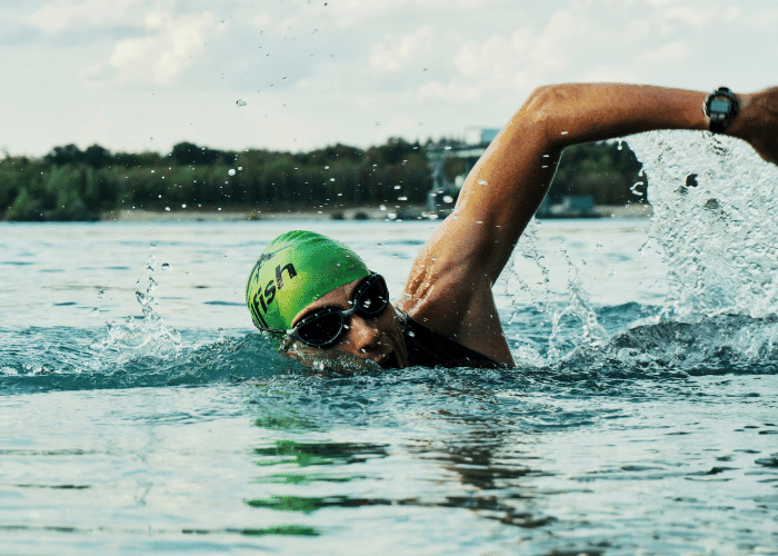 Man swimming in a lake with a green swimming hat and goggles