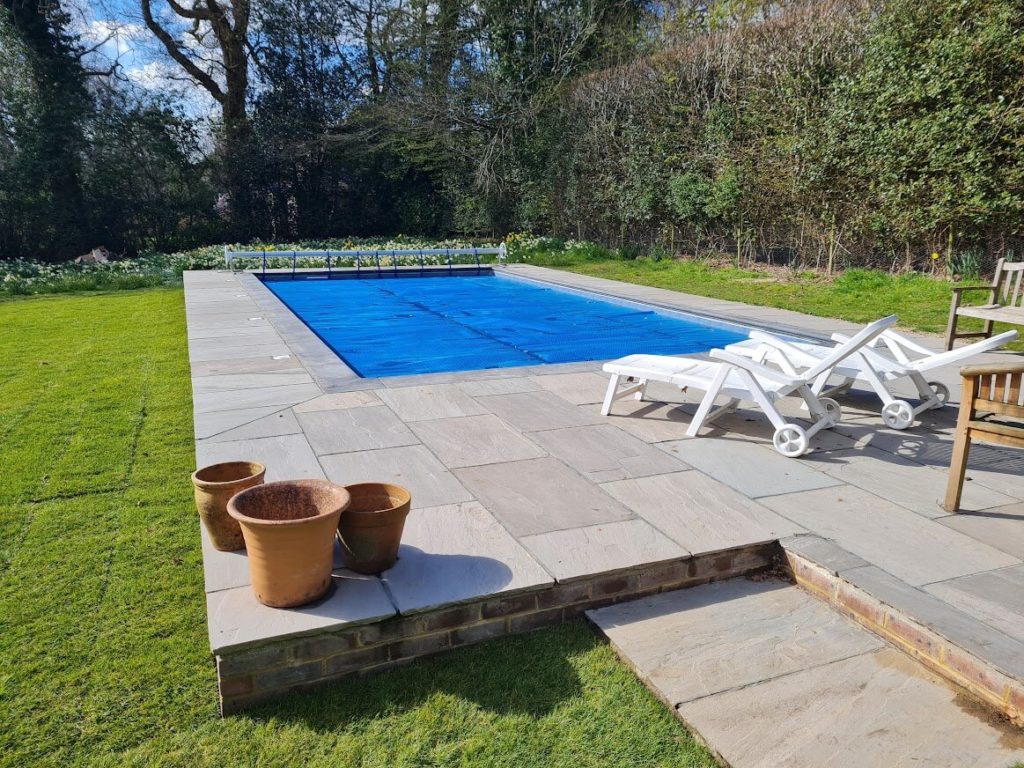 Outdoor swimming pool with plastic sunbeds, plant pots and a patio