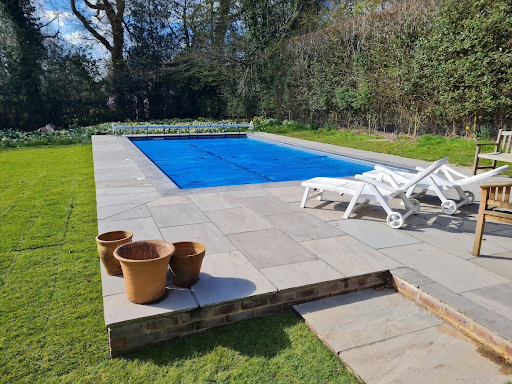 Rectangle outdoor swimming pool with blue swimming pool cover and patio with sunbeds and plant pots