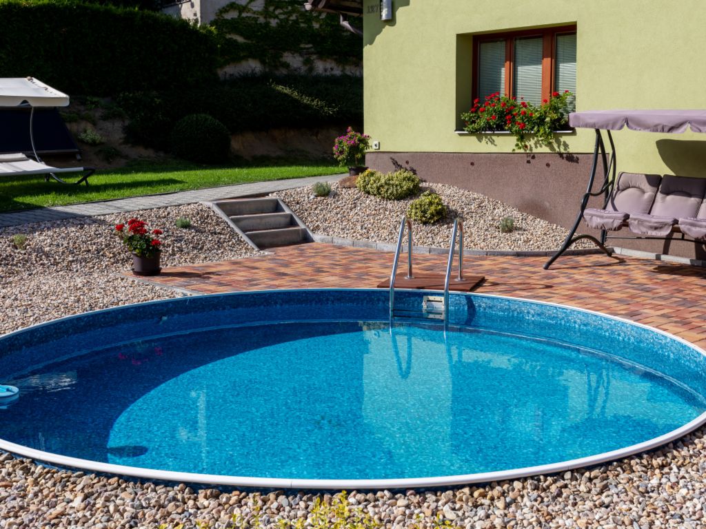 Round swimming pool in a back garden with seating and a patio