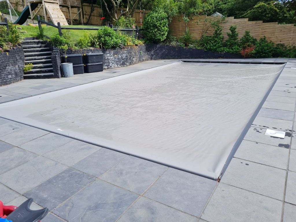 Grey swimming pool safety cover on an outdoor swimming pool