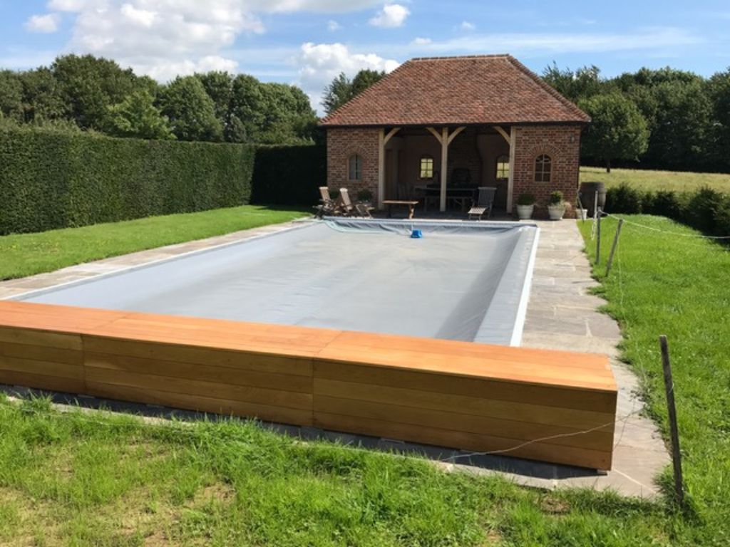 Grey swimming pool cover and oak storage box on an outdoor swimming pool with a brick out building