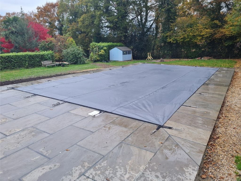 Dark grey winter debris swimming pool cover on an outdoor swimming pool in a back garden