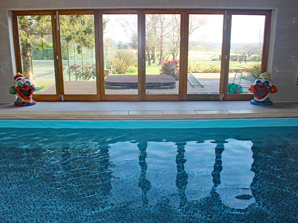 Indoor swimming pool looking out of bifold doors to a hot tub sunken into the ground
