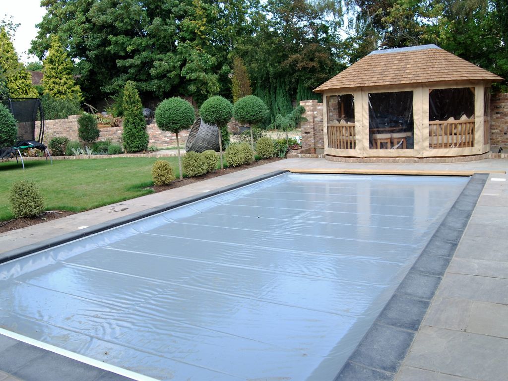 Grey pool safety cover on a swimming pool with wooden outbuilding