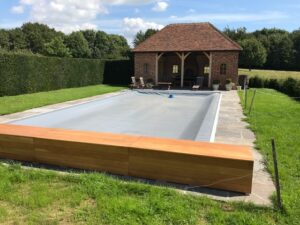 Grey swimming pool cover on an outdoor swimming pool with a brick outbuilding