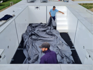 Two men fitting a swimming pool liner into a new pool construction