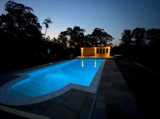 Finished swimming pool at night with lights on and an outbuilding