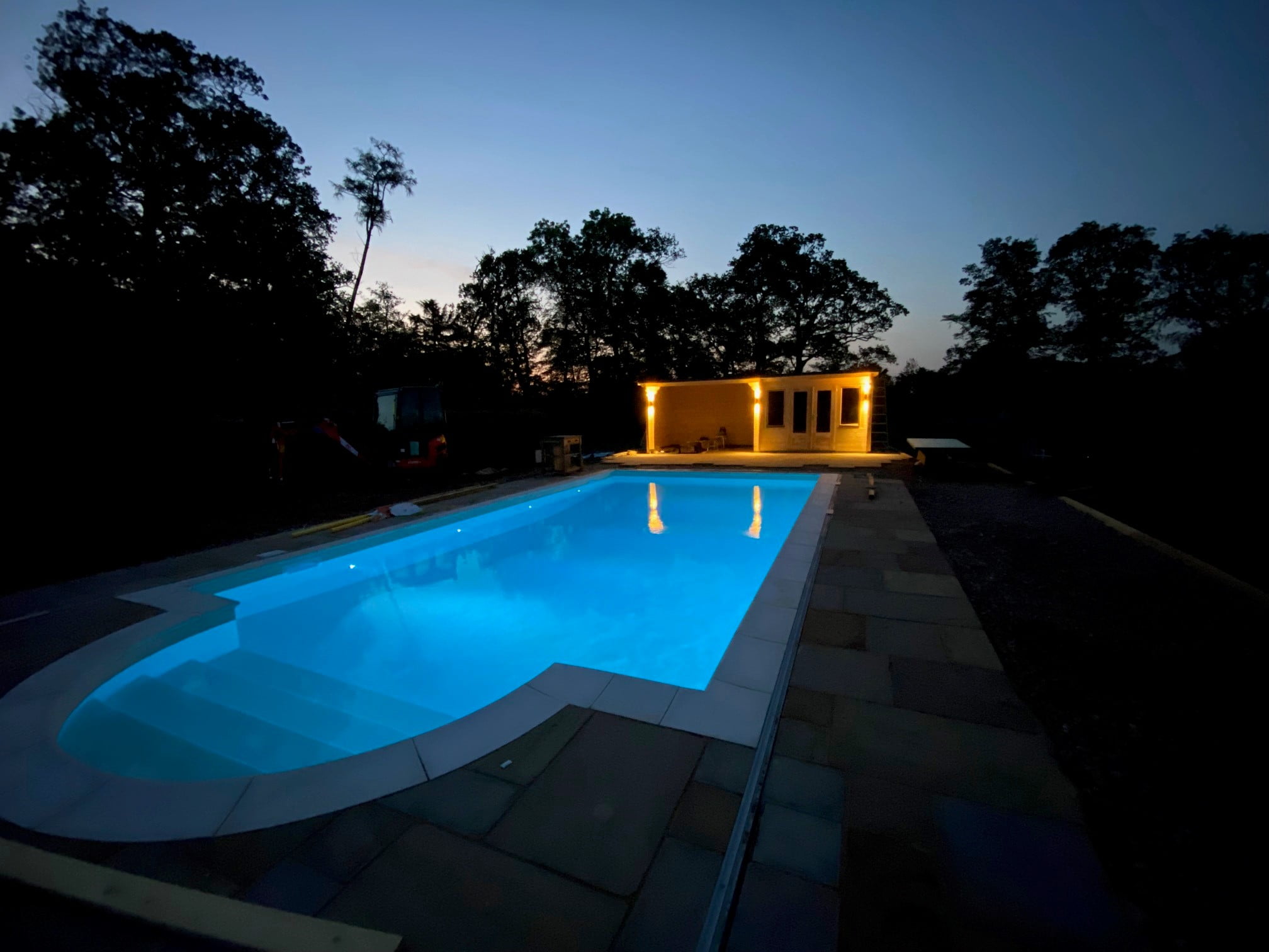 Finished swimming pool at night with lights on and an outbuilding