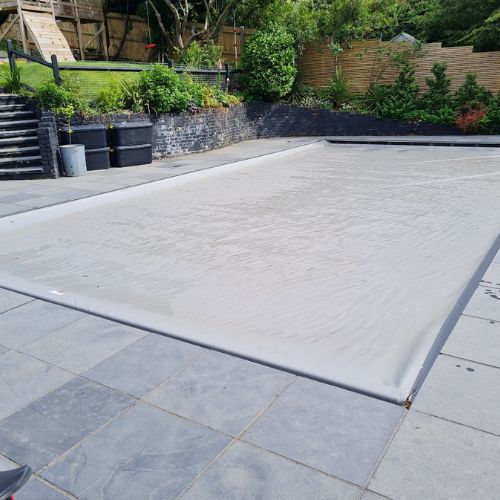 grey swimming pool cover over pool in garden