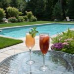 two cocktail glasses on round glass patio table with a swimming pool in the background